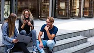 Stock image of three young adults making use of BYOD in their institution and using their own devices whilst mobile, on and off campus.